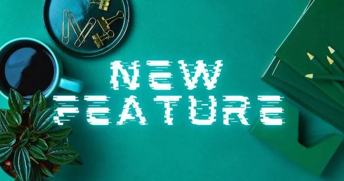 Image of desk with a cup, paper pins, a notebook and the text in the middle: New Feature