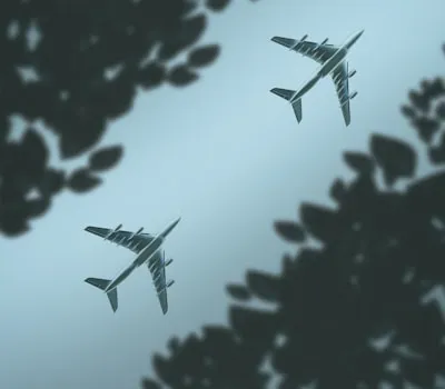 two airplanes flying in the sky above trees
