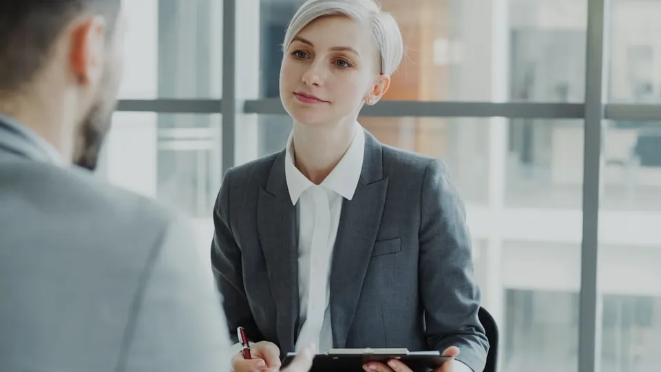 Woman in suit interviews man at desk