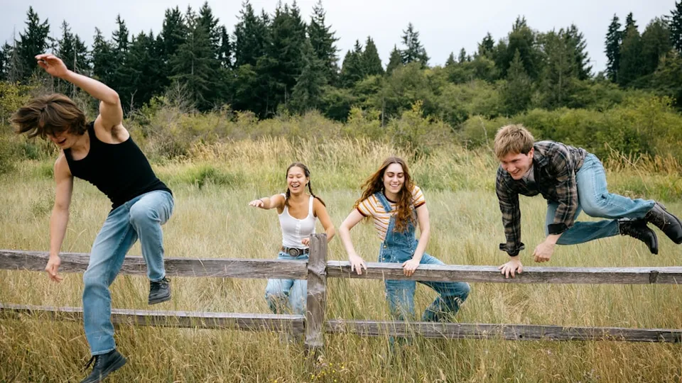 Four friends climbing over a wooden fence outdoors