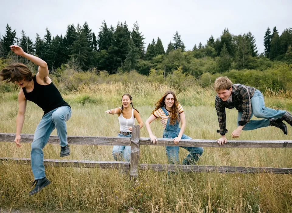 Four friends climbing over a wooden fence outdoors